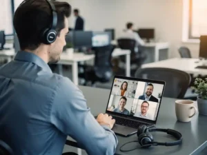 Professional aan modern bureau met laptop waarop videovergadering loopt en USB-headset, open kantoor op de achtergrond.